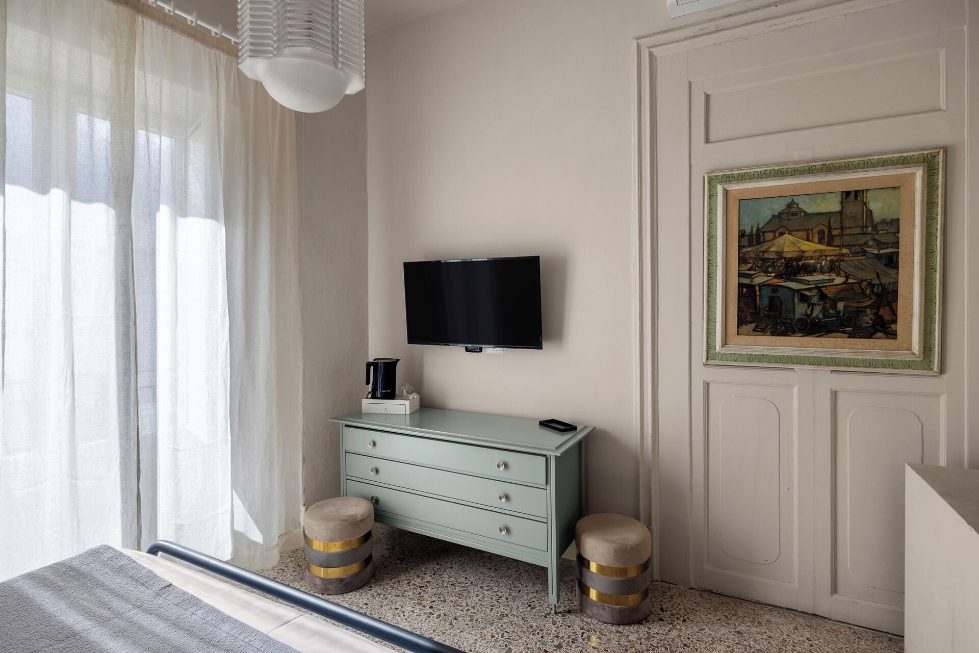 Una habitación con un televisor montado en la pared, un candelabro, un cuadro enmarcado, un aparador verde y dos taburetes.
