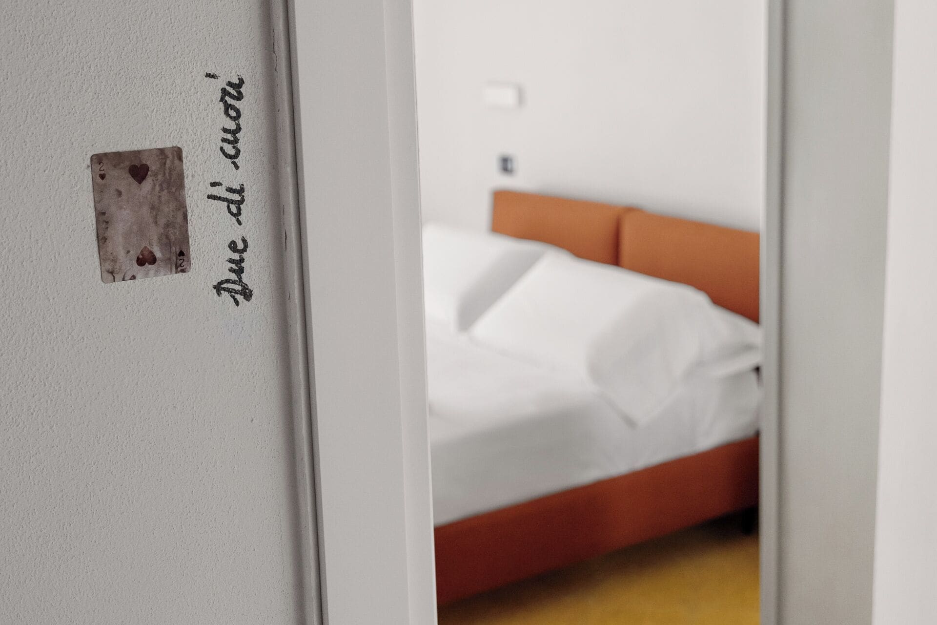 A bedroom with a bed, a white wall, and a small square object with text.