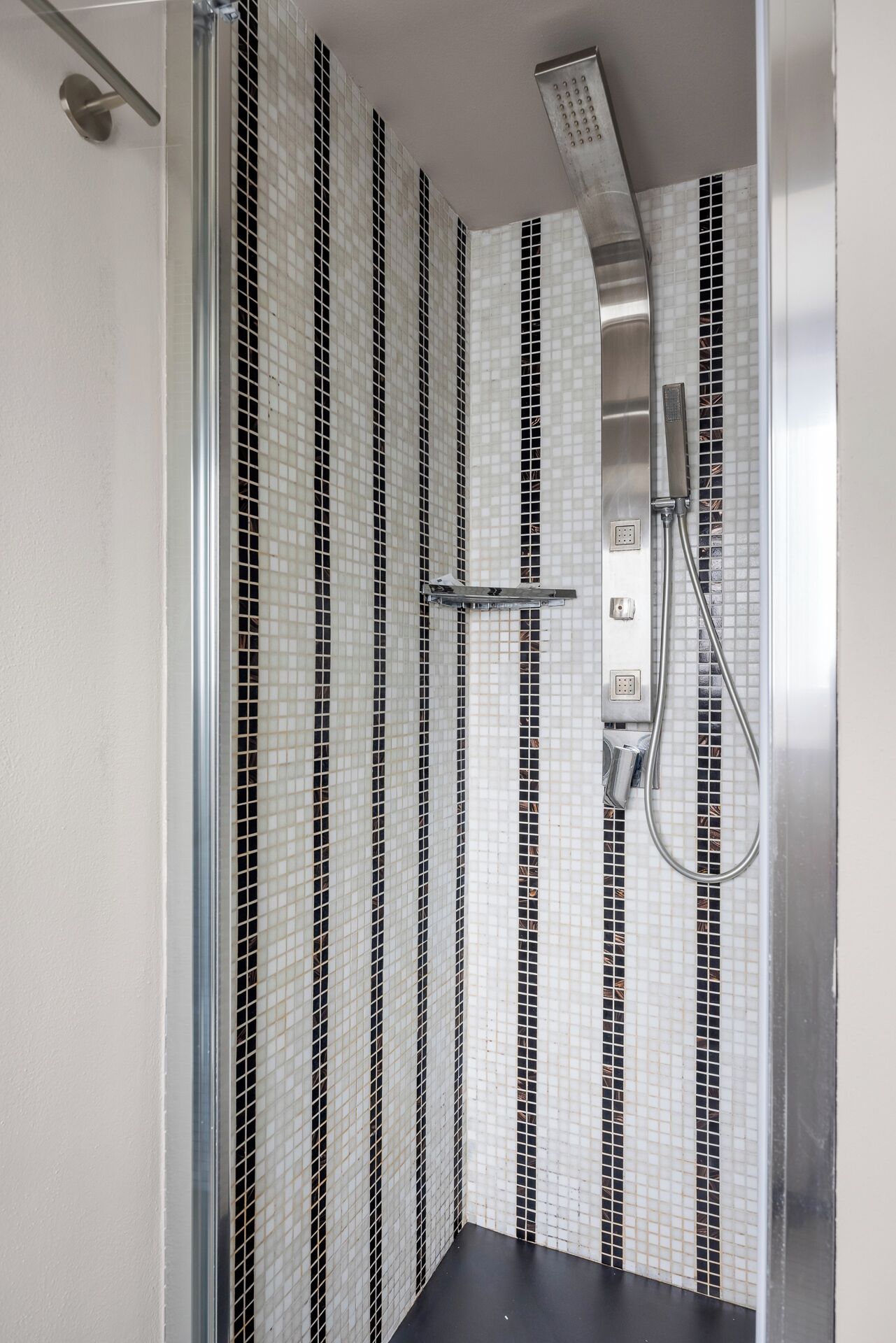 Une douche dotée d’une porte en verre, d’un pommeau de douche à main et d’un mur orné d’un motif de carreaux noirs et blancs.