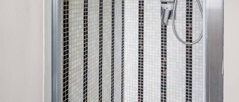 Une douche dotée d’une porte en verre, d’un pommeau de douche à main et d’un mur orné d’un motif de carreaux noirs et blancs.