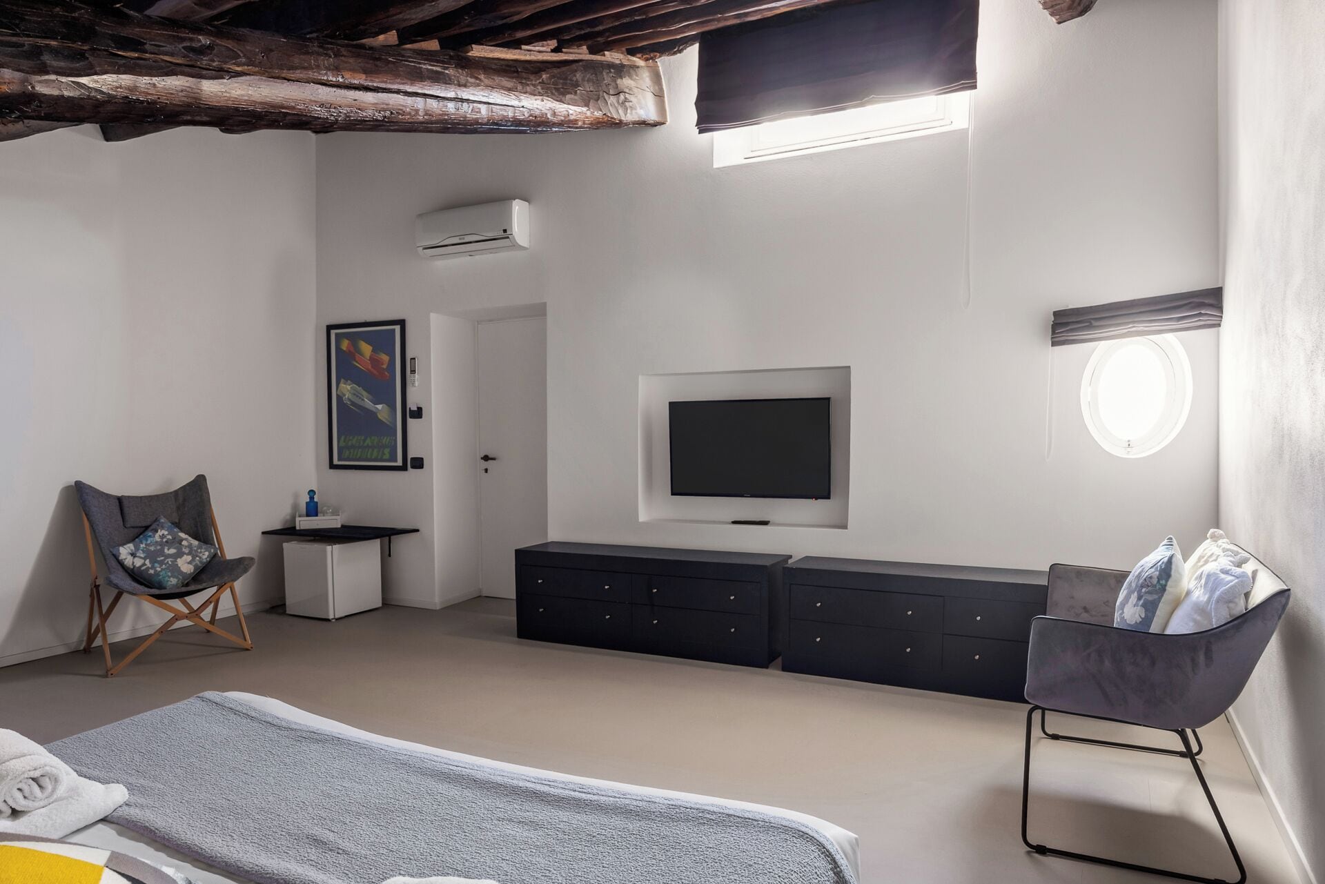 Quarto com cama, televisão, penteadeira, cadeira e janela.