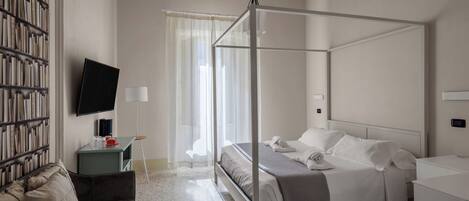 Une chambre d’hôtel moderne avec un lit à baldaquin, un téléviseur à écran plat, une bibliothèque et une petite table avec une lampe.