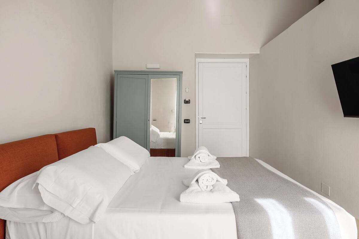 A hotel room with a bed, a wardrobe, a door, and a TV mounted on the wall.