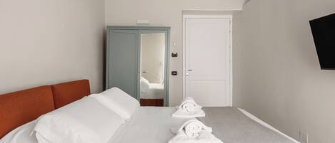 Una habitación de hotel con una cama, un armario, una puerta y un televisor montado en la pared.