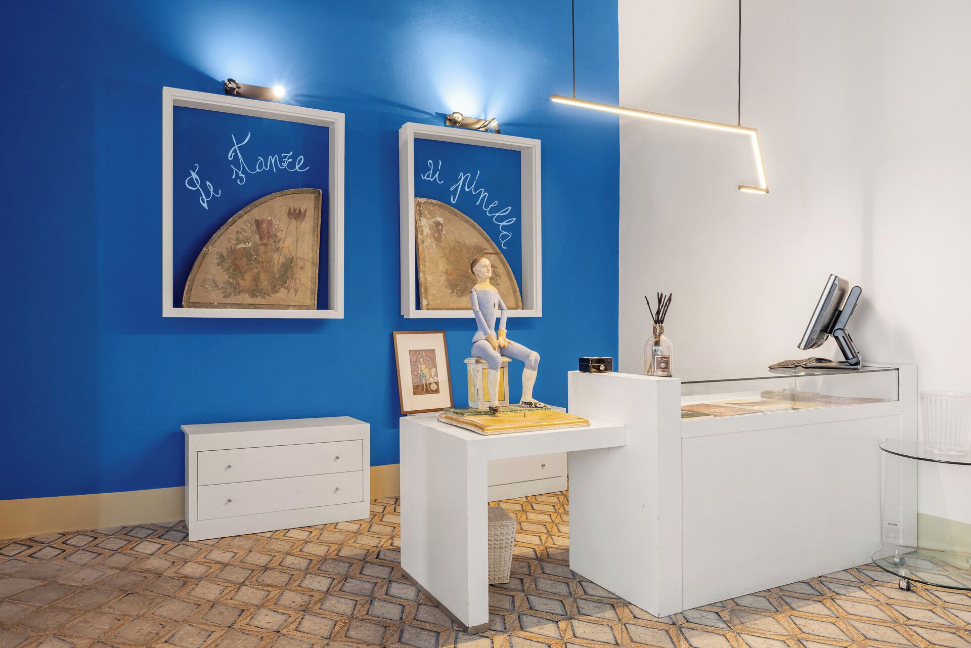 Un área de recepción con pared azul, obras de arte enmarcadas, un escritorio blanco y una vitrina de vidrio.
