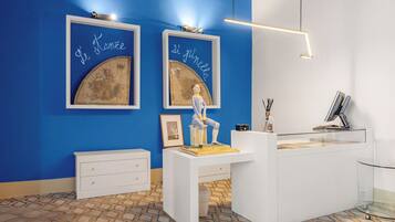 Un área de recepción con pared azul, obras de arte enmarcadas, un escritorio blanco y una vitrina de vidrio.