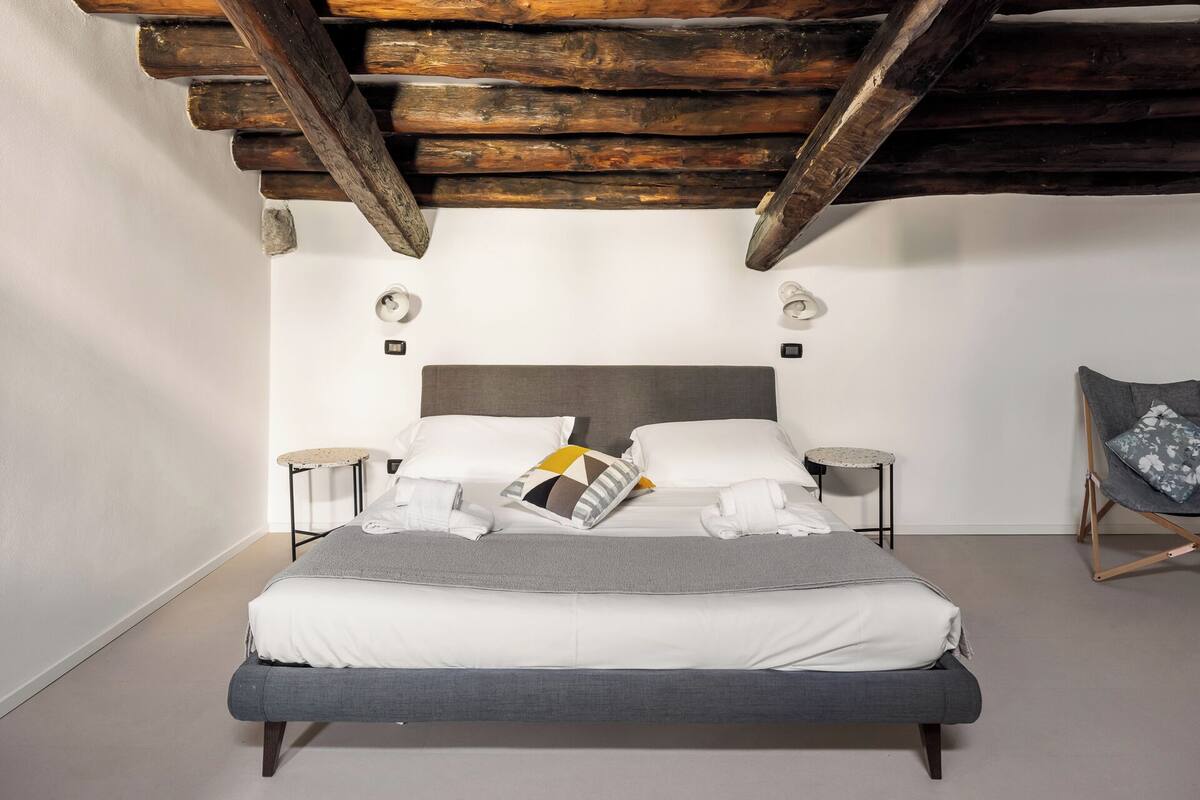 A bedroom with a bed, two bedside tables, a chair, and a wooden ceiling.