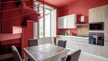 A modern kitchen with a red accent wall, a dining area with patterned tiles, and a staircase with red railings.