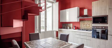 A modern kitchen with a red accent wall, a dining area with patterned tiles, and a staircase with red railings.