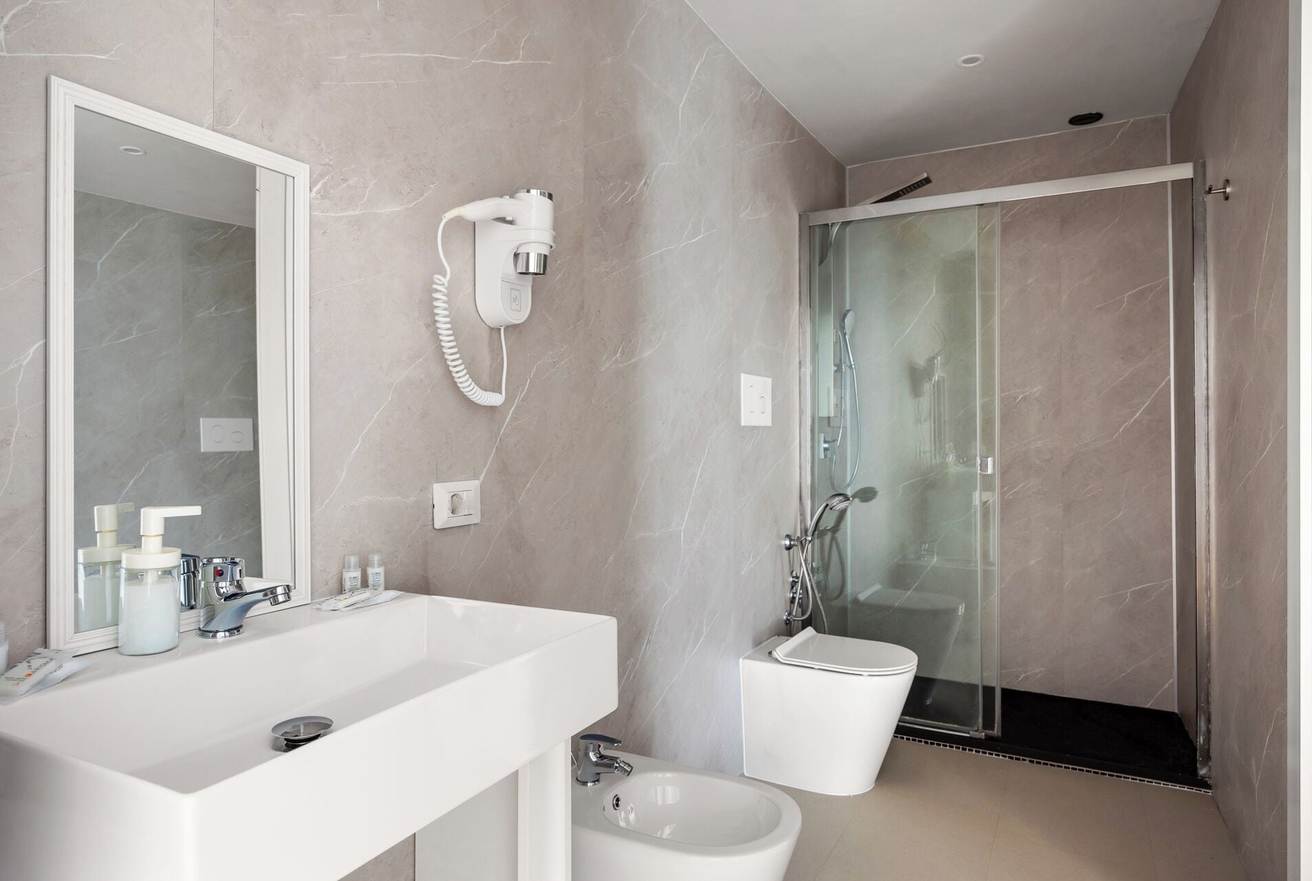 Une salle de bain moderne dotée d’un grand miroir, de deux lavabos, d’un bidet et d’une douche à parois de verre.