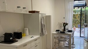 Uma cozinha moderna com armários brancos, uma área de jantar com mesa e cadeiras, e vista para o exterior através de uma porta de vidro.