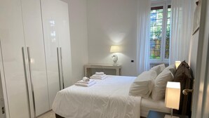 Quarto bem arrumado com cama, mesas de cabeceira, luminária e janela com vista.