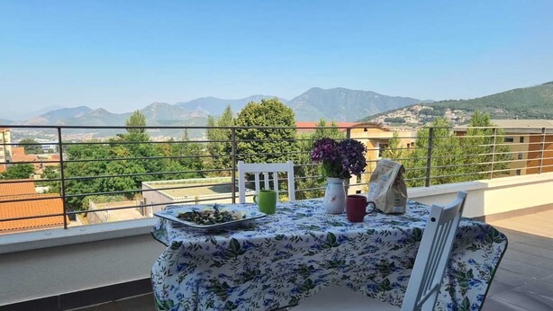 Ein Balkon mit Tisch für zwei Personen, einer Blumenvase und einer Tüte Snacks.