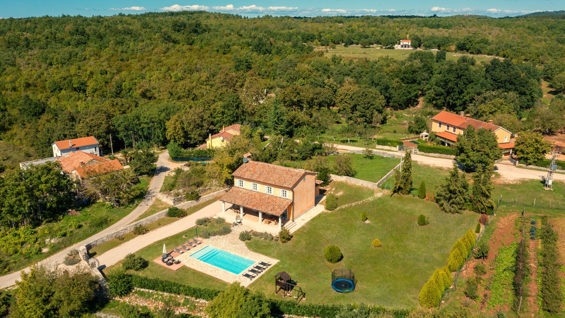 Une grande maison avec une piscine, entourée d’un paysage verdoyant luxuriant et d’une colline boisée en arrière-plan.