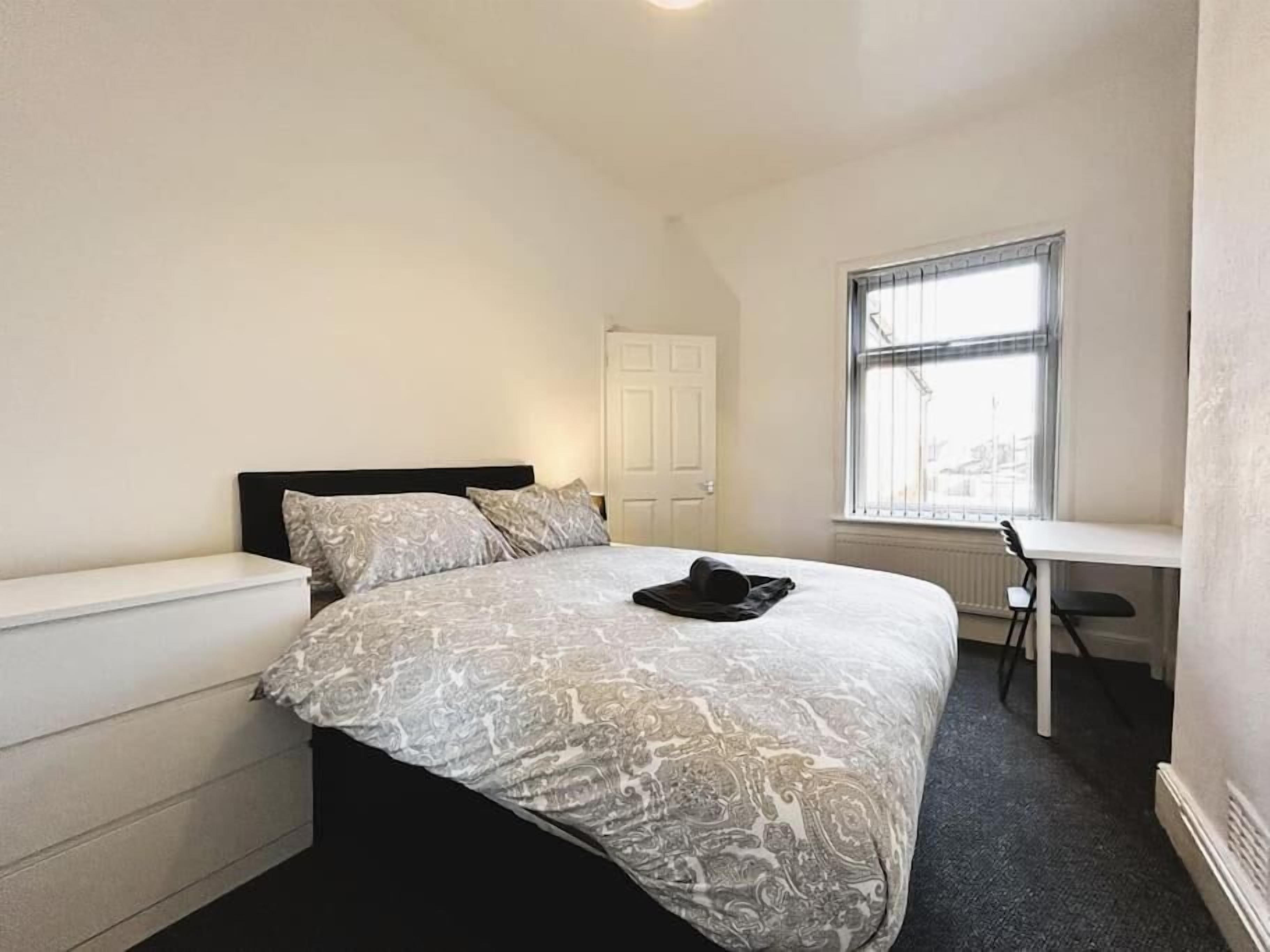 A bedroom with a bed, a desk, and a window.