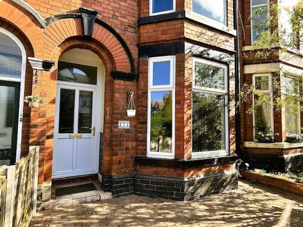 A brick house with a white front door, a bay window, and a number plaque.