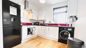 A modern kitchen with white cabinets, a black refrigerator, a microwave, a stove, and a washing machine. - Salisbury Place by SG Property Group (Crewe)