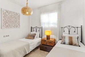 A bedroom with two single beds, a decorative wall piece, a hanging light fixture, and a bedside table with a lamp.