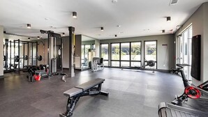 Un gimnasio amplio con diversos equipos de ejercicio, ventanas grandes y un diseño moderno.