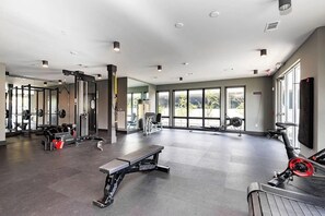 Ein großzügiger Fitnessraum mit verschiedenen Trainingsgeräten, großen Fenstern und einem modernen Design.