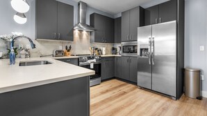 Una cocina moderna con gabinetes grises, electrodomésticos de acero inoxidable, una isla central y piso de madera.