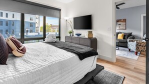 Un dormitorio moderno con una cama grande, un televisor de pantalla plana y vistas a edificios a través de amplios ventanales.
