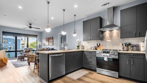 Una cocina moderna con gabinetes oscuros, electrodomésticos de acero inoxidable e iluminación colgante.