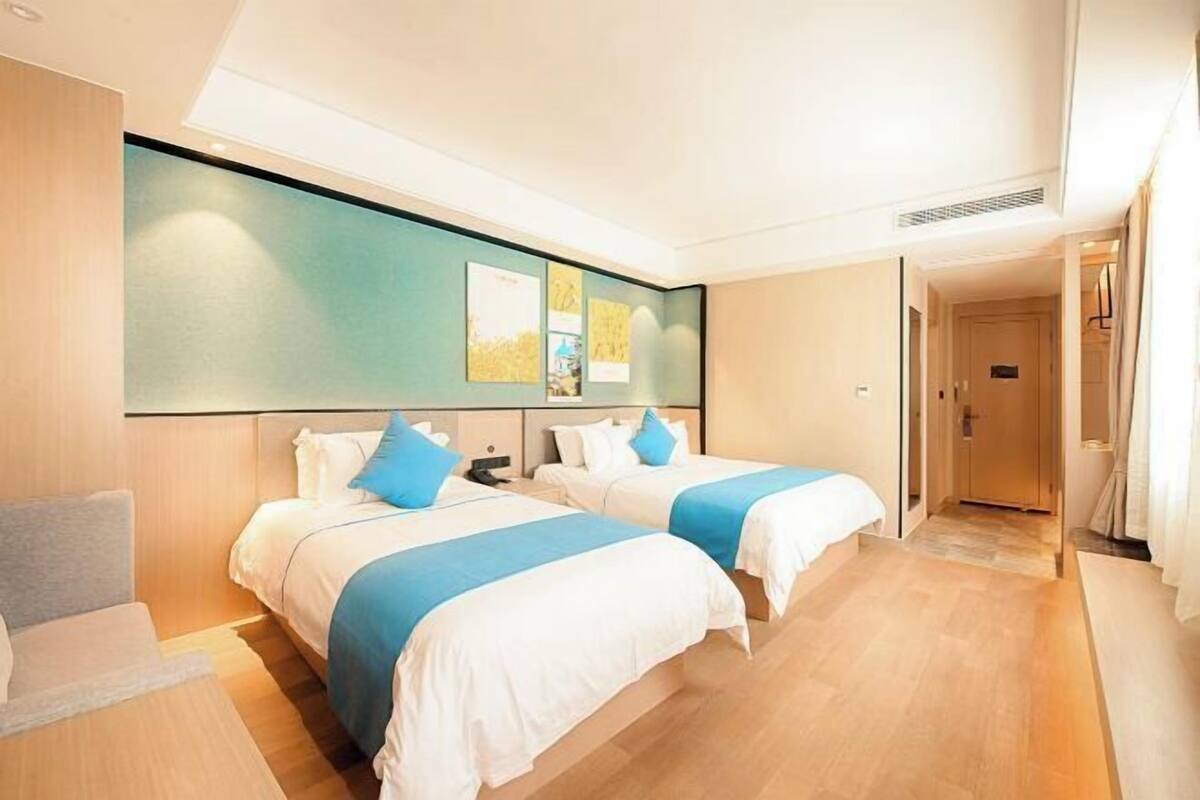 A hotel room with two beds, a sofa, a large window, and a door leading to another room.