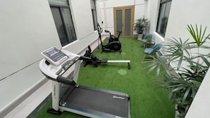 A small indoor gym with a treadmill, stationary bike, and exercise bench. There are potted plants and a door in the background. - BOOEIN HOTEL (Suzhou)