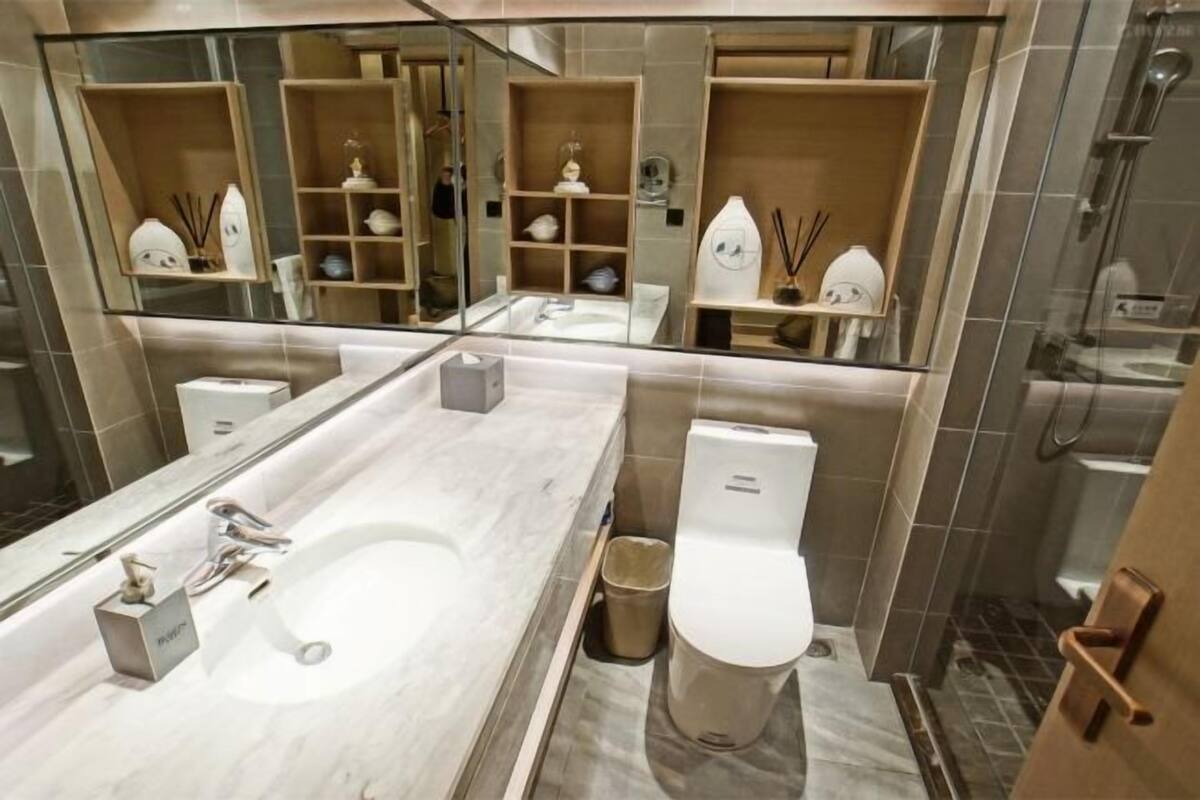 A modern bathroom with a large mirror, a marble sink, a toilet, and shelves with toiletries.