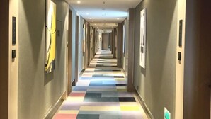 A hotel corridor with a colorful floor, framed artwork on the walls, and a long, straight layout. - BOOEIN HOTEL (Suzhou)