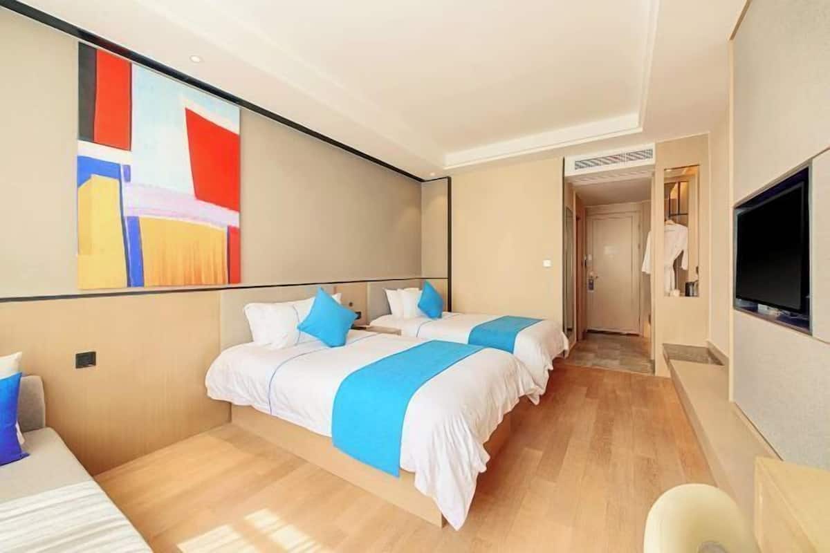 A hotel room with two beds, a TV, and a painting on the wall.