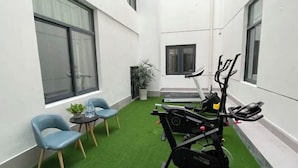 A small, enclosed workout area with a treadmill, elliptical, and stationary bike, surrounded by artificial grass and two blue chairs. - BOOEIN HOTEL (Suzhou)