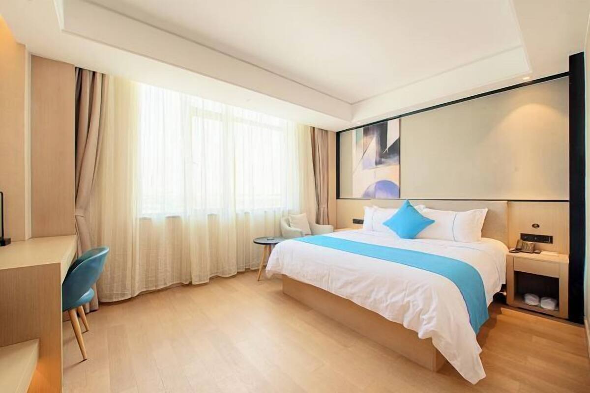 A hotel room with a bed, a desk, a chair, a nightstand, and a window with curtains.