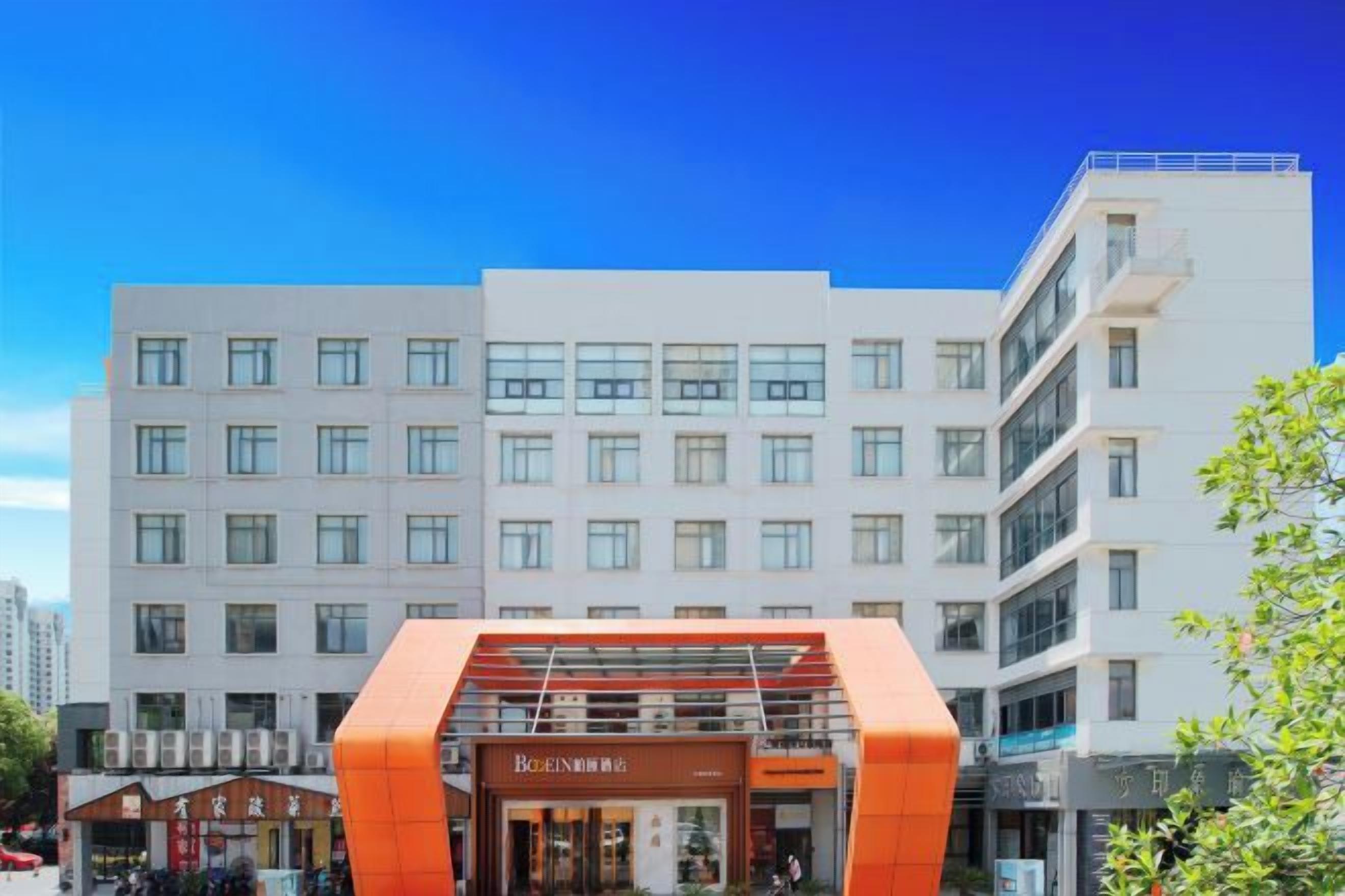 Un hotel urbà de diverses plantes amb un disseny modern, destacant una entrada taronja i oferint una vista clara de l'entorn.