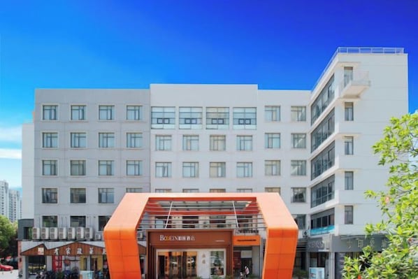 Ein mehrstöckiges Hotel mit modernem Design, das durch einen auffälligen orangefarbenen Eingang und einen klaren Blick auf die umliegende Stadtlandschaft gekennzeichnet ist.