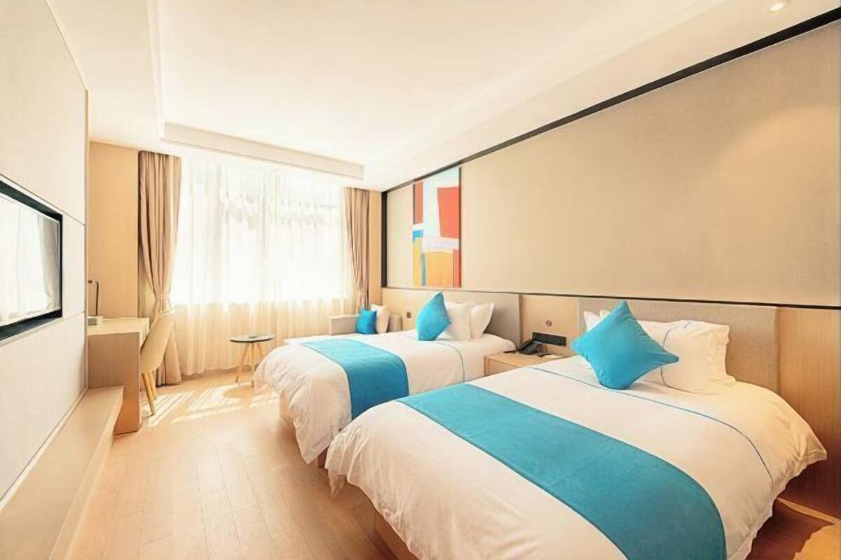 A hotel room with two beds, a desk, and a large window with curtains.