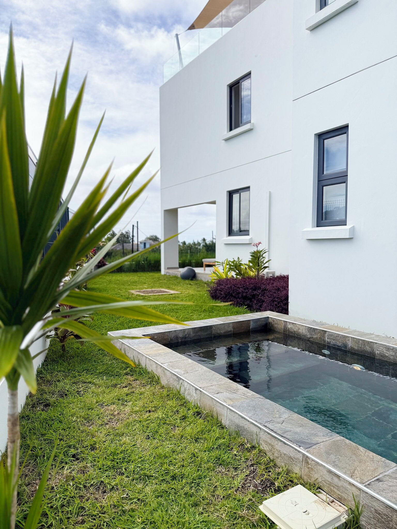 A modern two-story building with a swimming pool, surrounded by a well-maintained lawn and various plants.