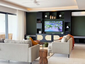 A modern living room with a large flat-screen TV, grey sofas, a wooden coffee table, and a ceiling fan. - North Island View by LOV Mauritius  (Grand Gaube)