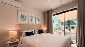 A hotel room with a large bed, two bedside lamps, a ceiling fan, and a view of the outdoor seating area.