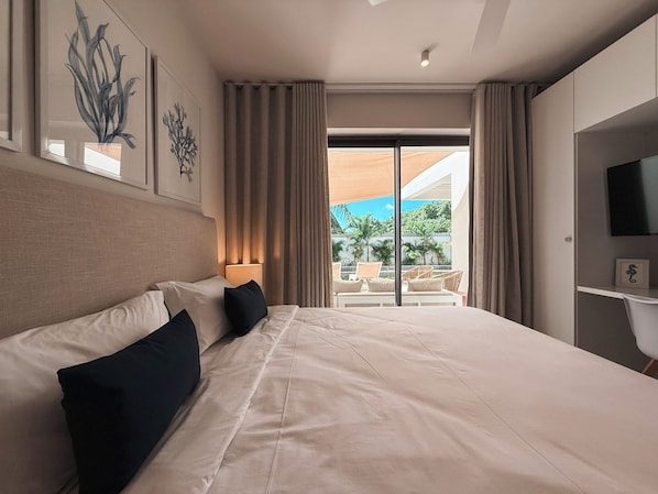 A hotel room with a large bed, a TV, a desk, and a balcony with outdoor furniture.