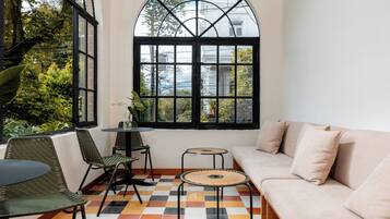 Una habitación con piso a cuadros, un sofá, dos sillones, una mesita y un amplio ventanal de arco con vistas a zonas verdes y edificios.