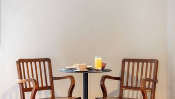 Una mesa redonda pequeña con dos sillas de madera, una taza, un plato con comida y un vaso de jugo de naranja.