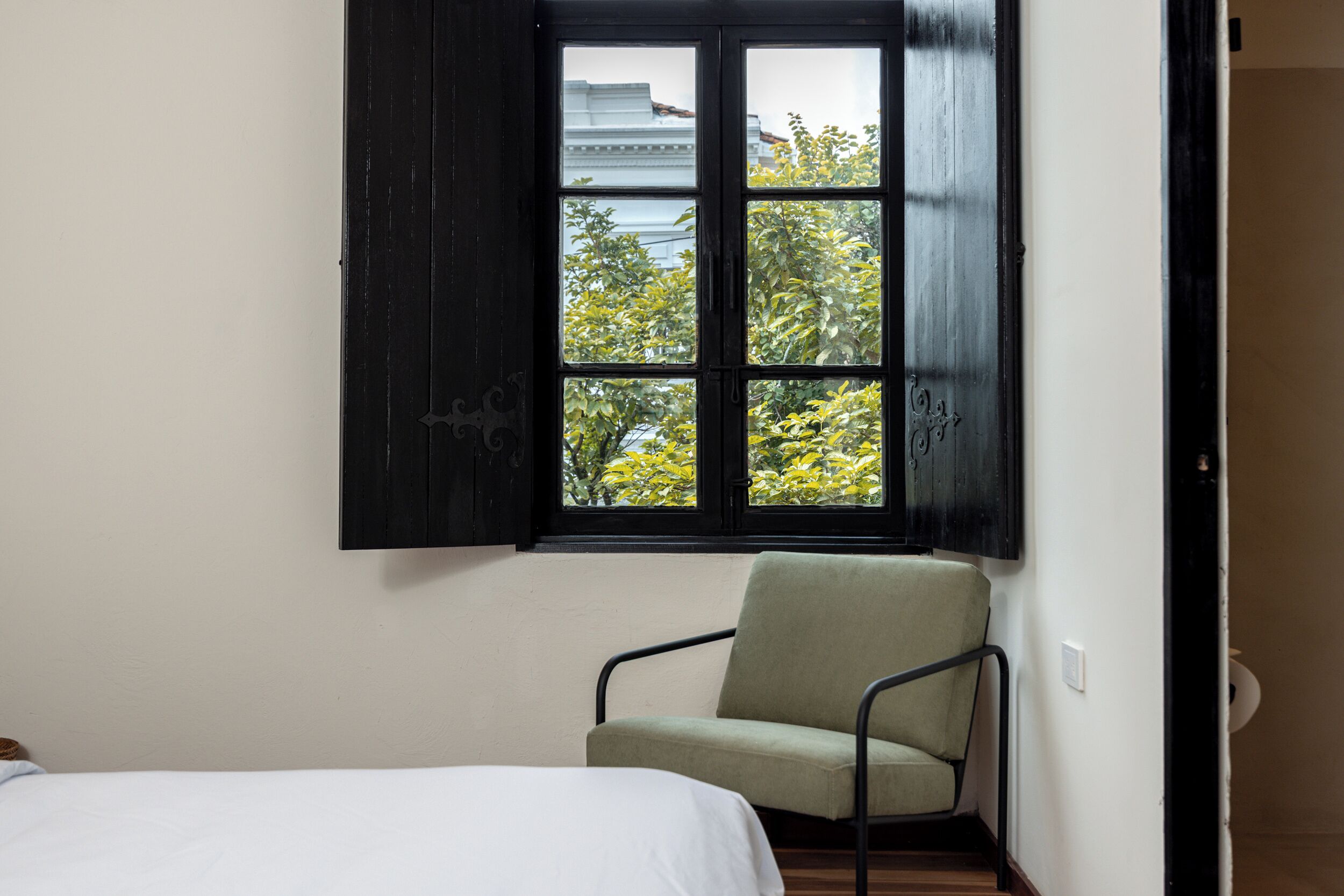 Ein Zimmer mit Bett, Stuhl und Fenster mit Blick auf Bäume und Gebäude.