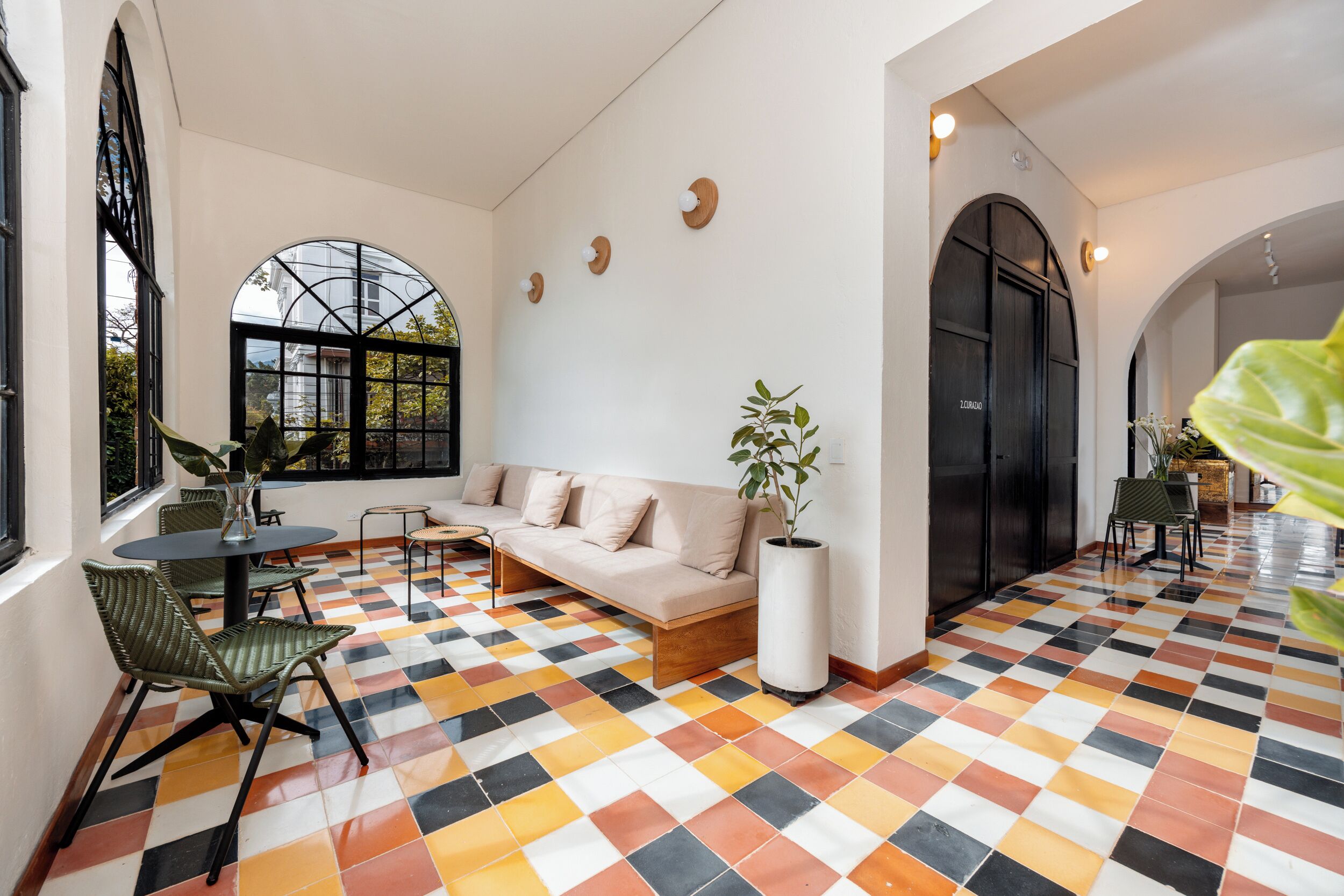 A room with a checkered floor, a sofa, a dining table with chairs, and a large window.