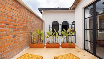 Un patio con muro de ladrillo, tres plantas en macetas y dos sillas de mimbre.