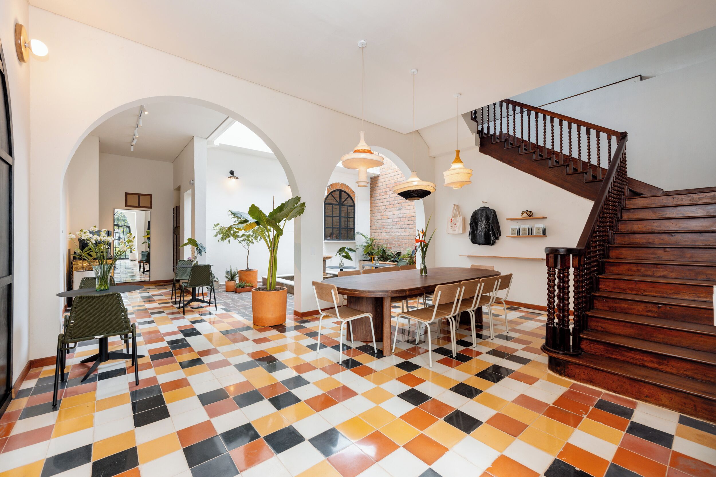 A spacious dining area with a checkered floor, a wooden staircase, and a brick wall.