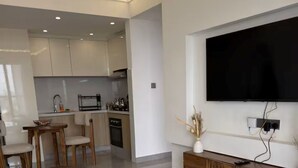 Ein modernes Wohnzimmer mit Flachbildfernseher, Couchtisch aus Holz und einem gemusterten Teppich.