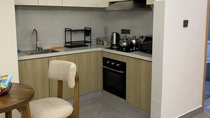 Eine moderne Küche mit hellen Holzschränken, einem schwarzen Geschirrspüler und einem Essbereich mit zwei Stühlen und einem kleinen Tisch.