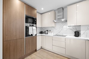 Eine moderne Küche mit Holzausstattung, einem Edelstahlbackofen, einer Kaffeemaschine und einer Marmor-Spritzschutzwand.